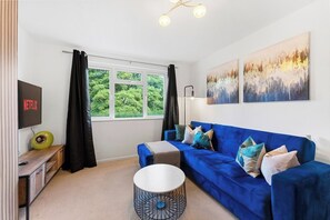 Ein modernes Wohnzimmer mit einem blauen Sofa, einem Couchtisch, einem Fernseher und Kunstwerken an der Wand.
