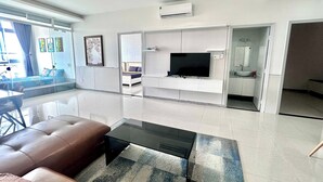 A modern living room with a sofa, a coffee table, a flat-screen TV, and a dining area with a table and chairs.