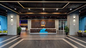 A modern hotel lobby with a reception desk, seating area, and large windows.