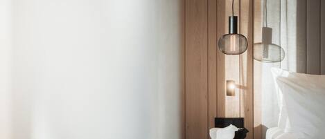 Un dormitorio moderno con una pared de madera, una mesa redonda de madera con una figurita de gato blanco, una silla negra y una lámpara colgante.