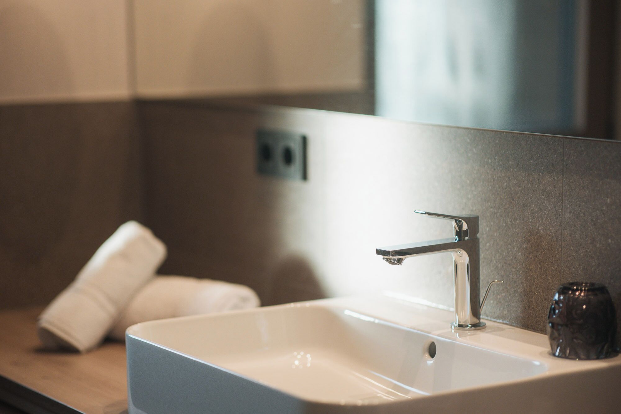 Een moderne badkamer met een rechthoekig wastafelmeubel, een enkele kraan en een klein glazen potje op het aanrecht.