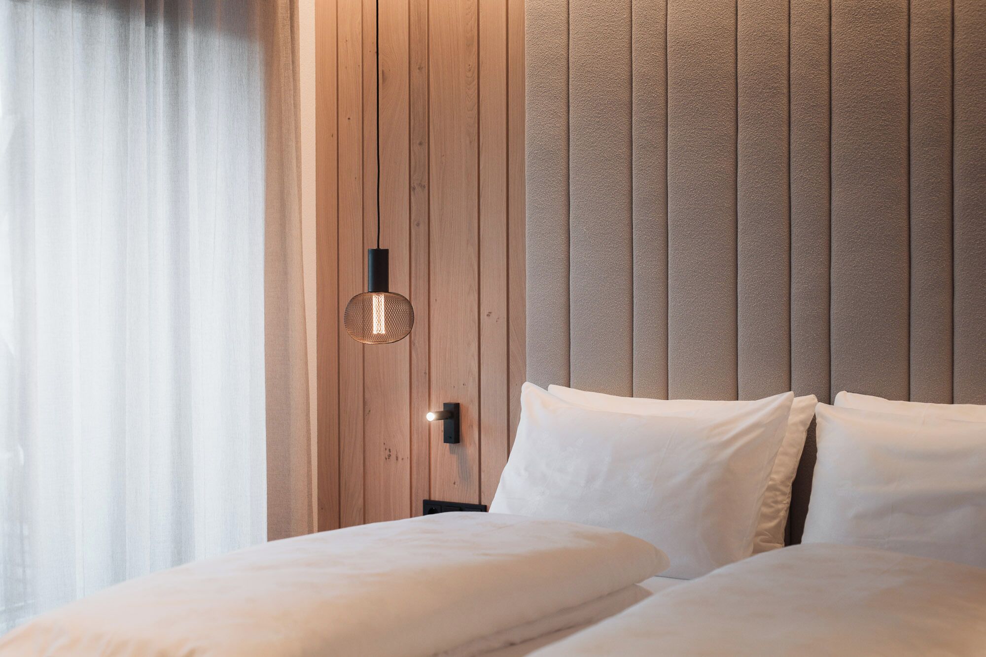 A bedroom with a wooden headboard, a bed with white linens, and a hanging light fixture.