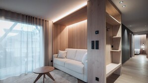 A modern living room with a white sofa, a round wooden table, and built-in wooden shelving. - Mountain Residence CLARA (Brunico)