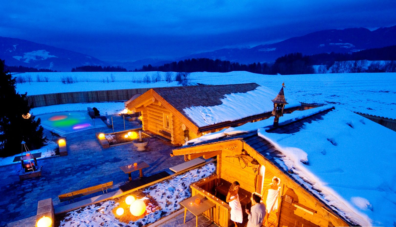 Eine Holzhütte mit Sauna, Sitzgelegenheiten im Freien und Blick auf eine verschneite Landschaft.