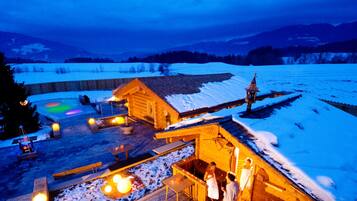 Eine Holzhütte mit Sauna, Sitzgelegenheiten im Freien und Blick auf eine verschneite Landschaft.