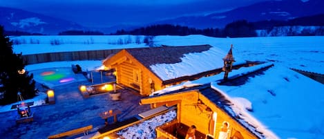 Una cabaña de madera con sauna, mobiliario exterior y vistas a un paisaje nevado.