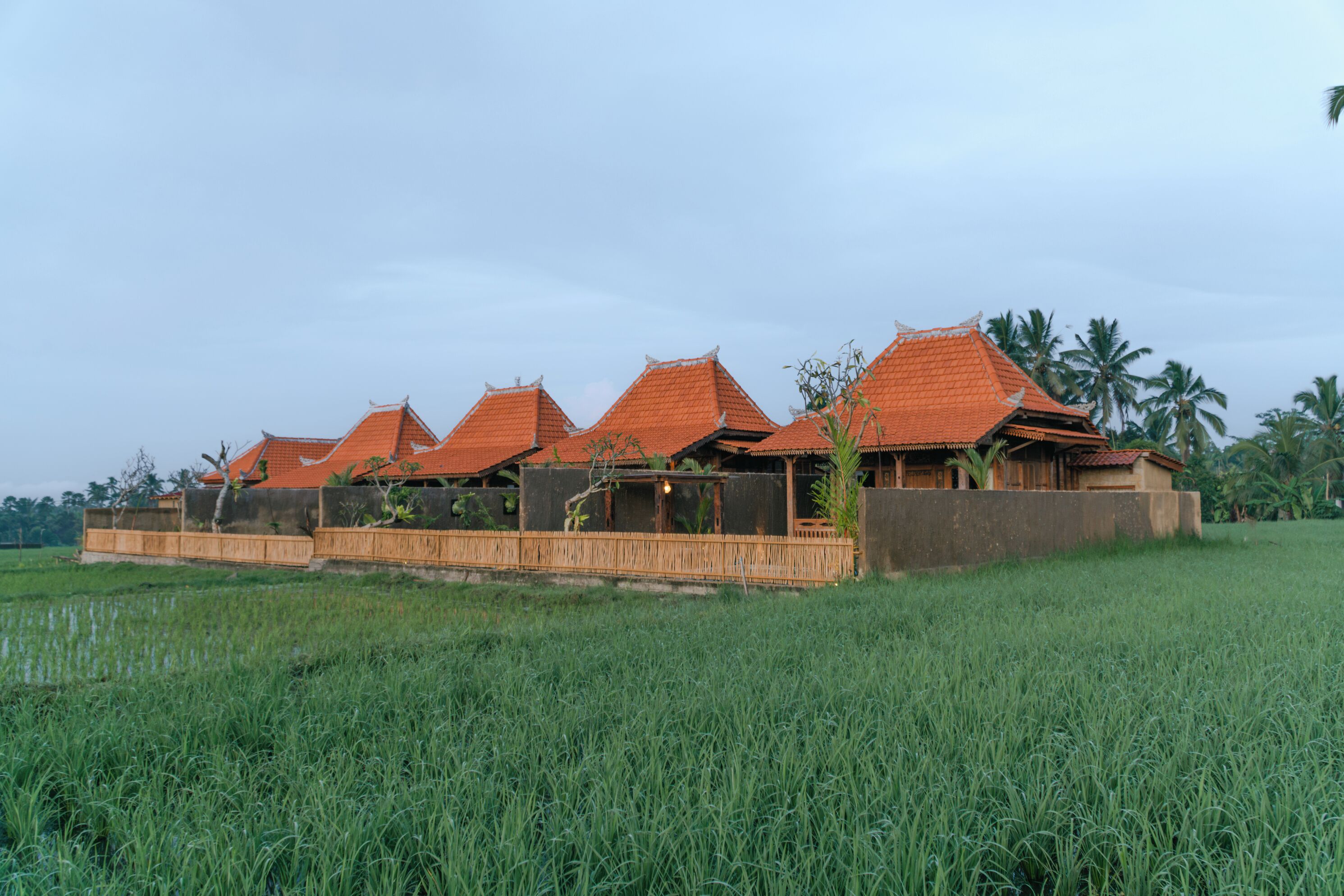 A row of traditional-style buildings with red-tiled roofs, situated in a lush green field.