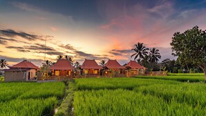 A row of traditional-style buildings with red roofs, surrounded by lush green rice fields, under a sunset sky. - Arindama Villa Ubud by Dhananjaya Hospitality (Sebatu)