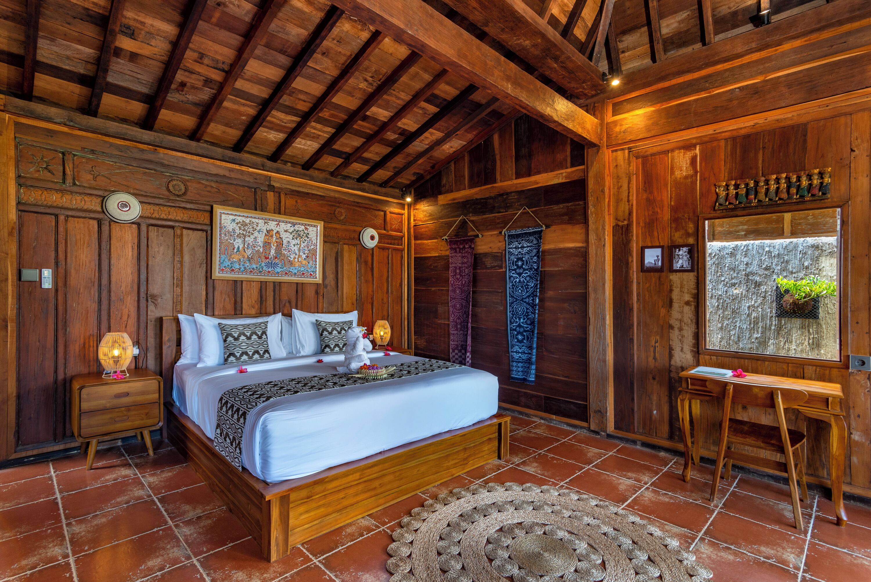 A wooden bedroom with a bed, nightstands, a desk, and a window with a plant.