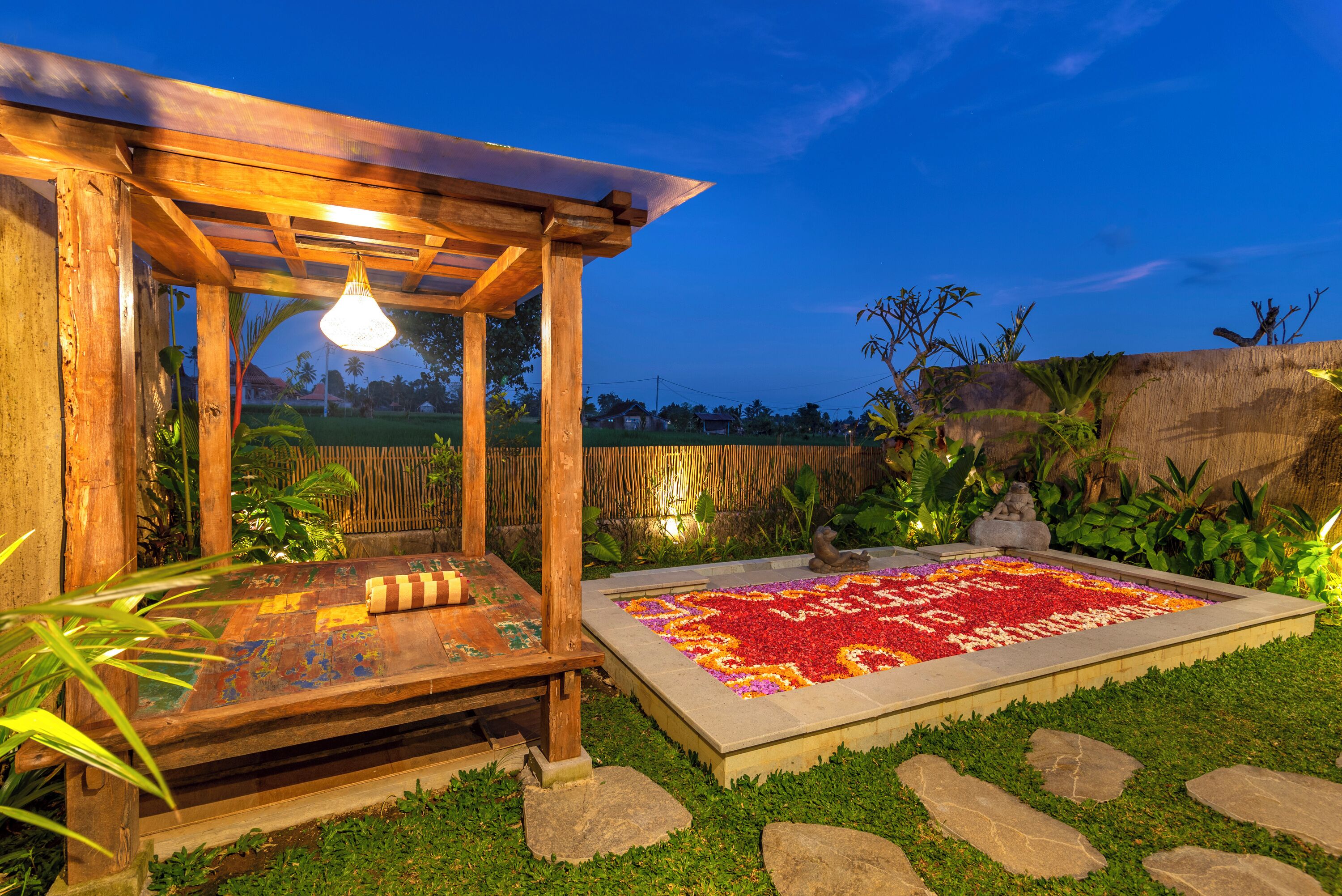 Une pergola en bois agrémentée d’un luminaire suspendu, d’un banc en bois à motifs et d’un parterre de fleurs rouges et jaunes.