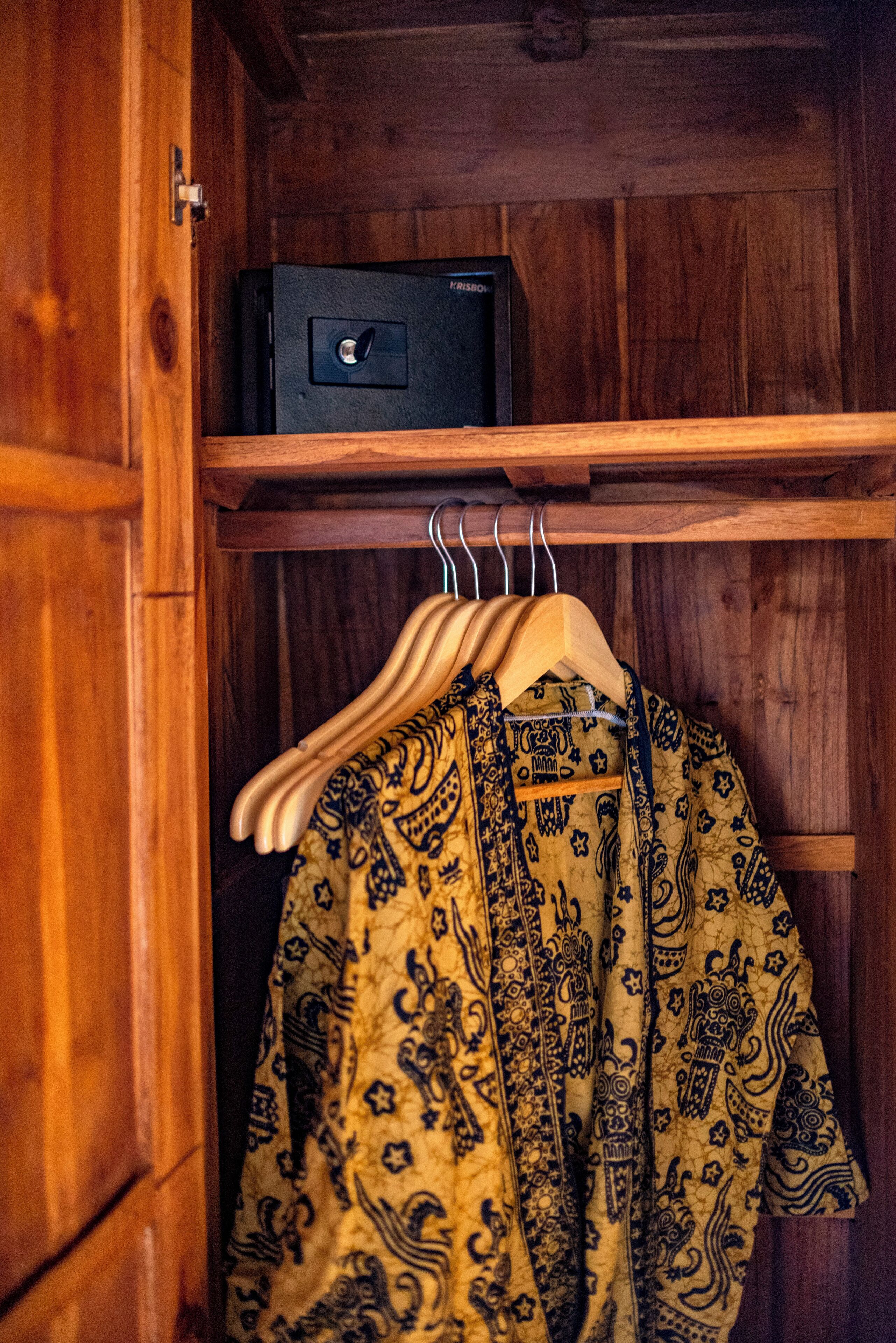 A wooden wardrobe with a hanging rack and a black safe.