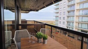 A balcony with a wooden table, two chairs, and two potted plants. - Studio by the Beach With Sea View (Koksijde)