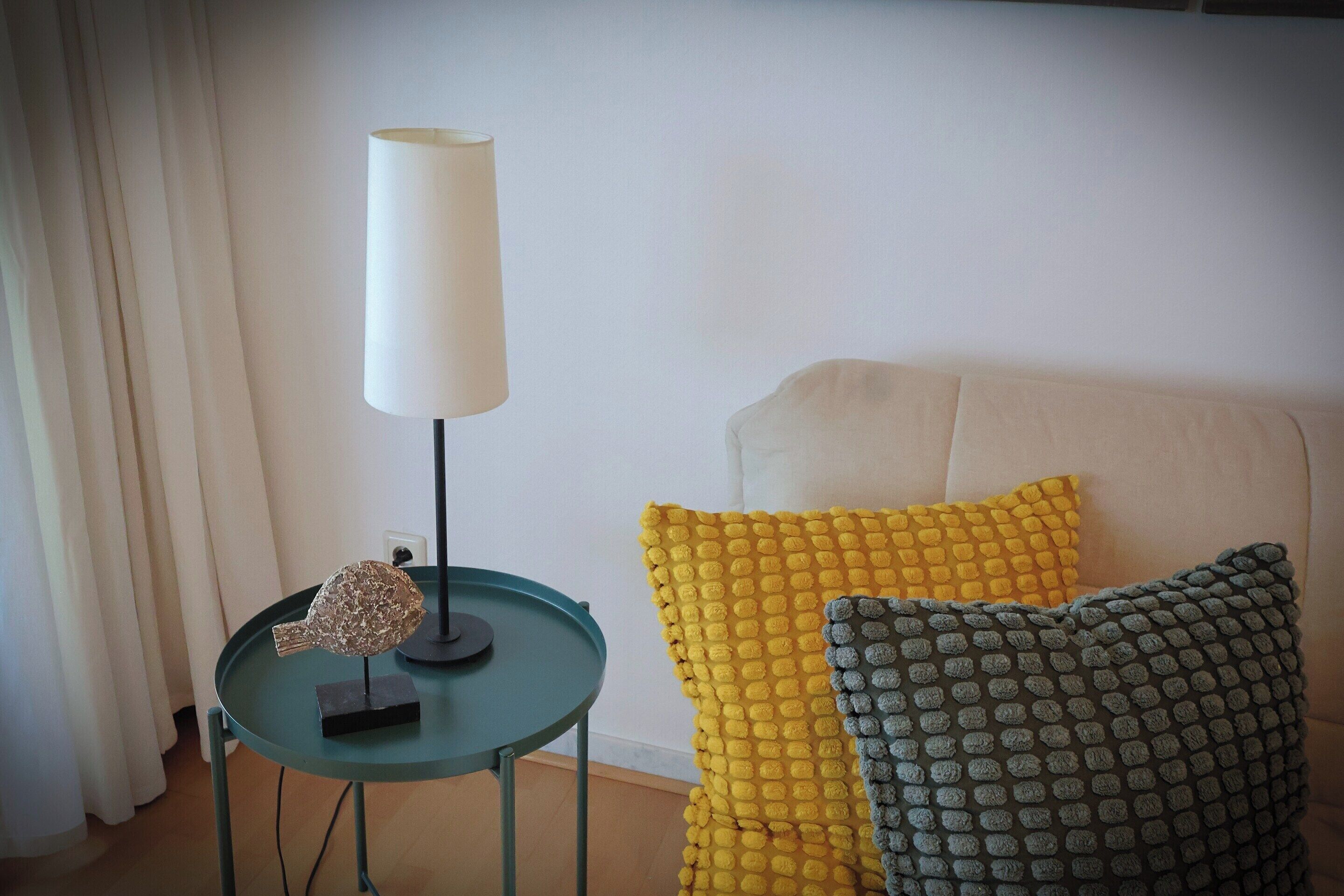 Une pièce avec une table ronde, une lampe et deux coussins sur un canapé.