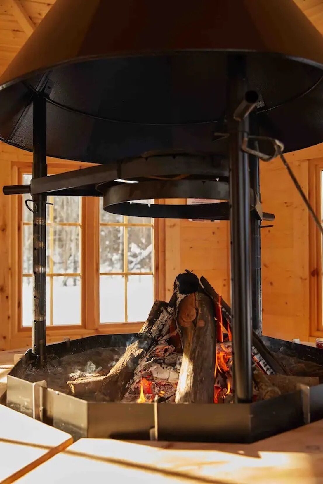 A wood-burning stove with a chimney, set in a room with wooden walls and a window.