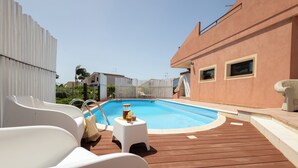 A swimming pool with a wooden deck, white lounge chairs, and a small table with a drink. - Villa Stephanie with pool (Marina di Ragusa)