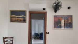 A room with a wooden chair, an air conditioner, a standing fan, and two framed artworks on the walls. - PO LAZISE HOUSE (Lazise)