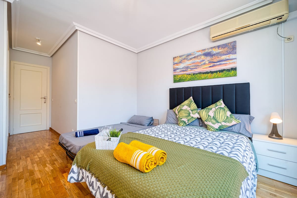 A bedroom with a bed, a nightstand, a lamp, a painting, and a door.