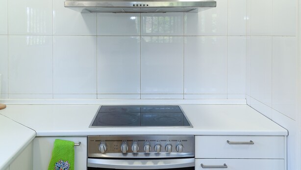 Une cuisine avec des carreaux blancs, une hotte de cuisine en acier inoxydable, un four encastré et une serviette verte accrochée à la porte du four.