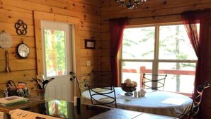 Eine Holzhütte mit Küchenzeile, ausgestattet mit Herd, Esstisch aus Holz und einem Fenster mit Vorhängen.