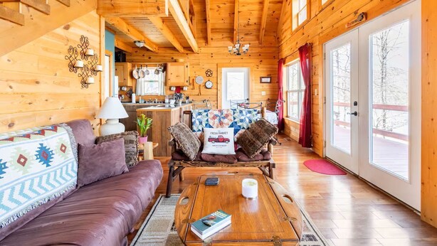 Ein gemütliches Blockhaus-Interieur mit Holzvertäfelung, einer Couch, einem Couchtisch und einem durchgehenden offenen Tür sichtbar liegenden Küchenbereich.