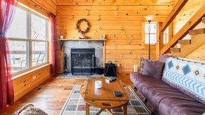 Ein gemütliches Blockhaus-Interieur mit Kamin, Holzwänden, einer Couch und einem Esstisch.