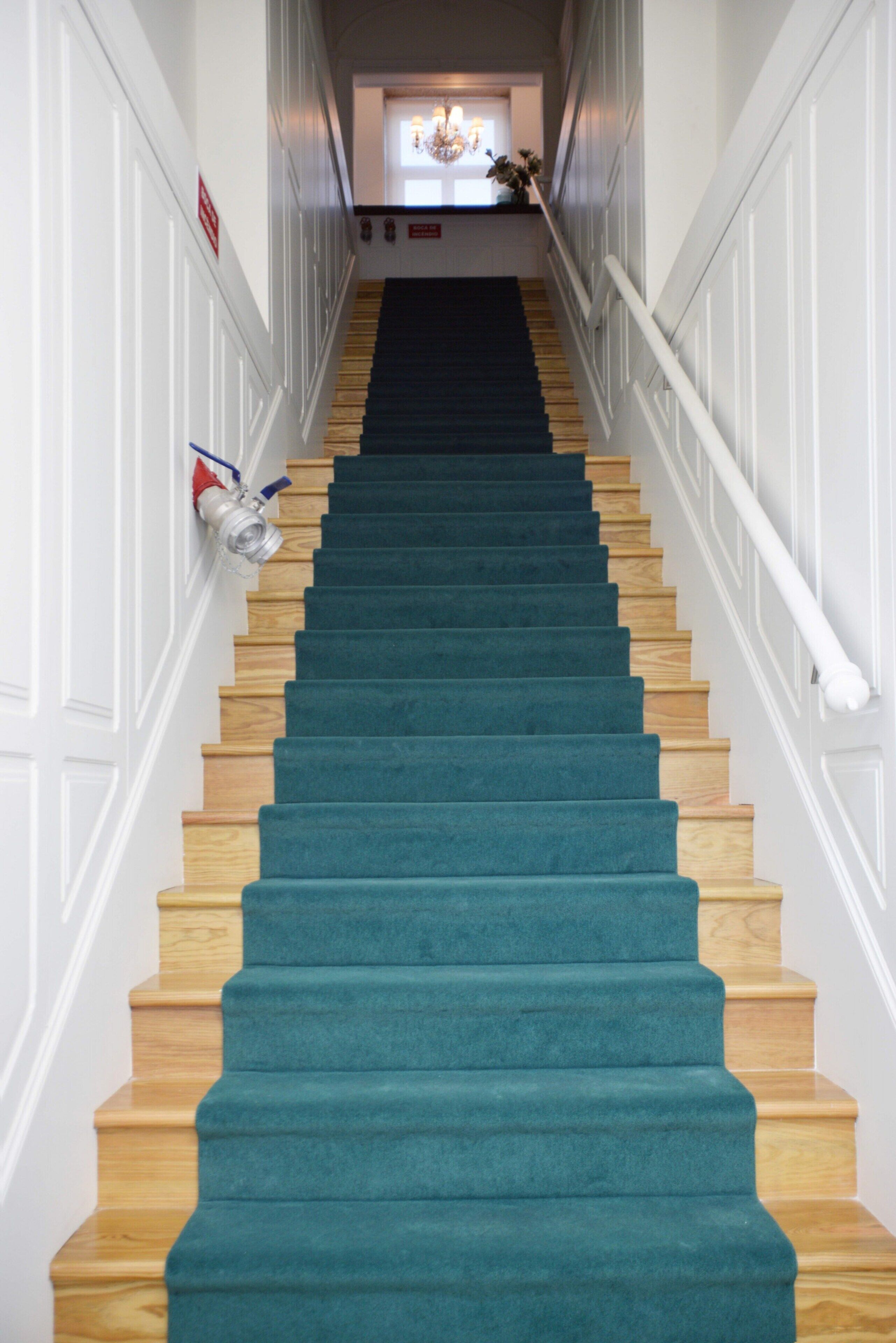 A staircase with wooden steps and teal carpet, leading to a landing with a chandelier.