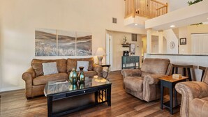 A spacious living room with a brown leather sofa, a glass coffee table, and a brown armchair. There is a wooden staircase leading to an upper level. - Meadow Brook Resort Getaway (Branson)