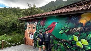 A mural with a lion, birds, and cyclists on a building with a tiled roof.