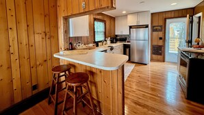 Una cocina con paredes de madera, una isla central con taburetes, un refrigerador y un fregadero.