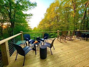 Relax on the deck surrounded by lush greenery, with a fire pit and comfortable seating for a peaceful retreat.