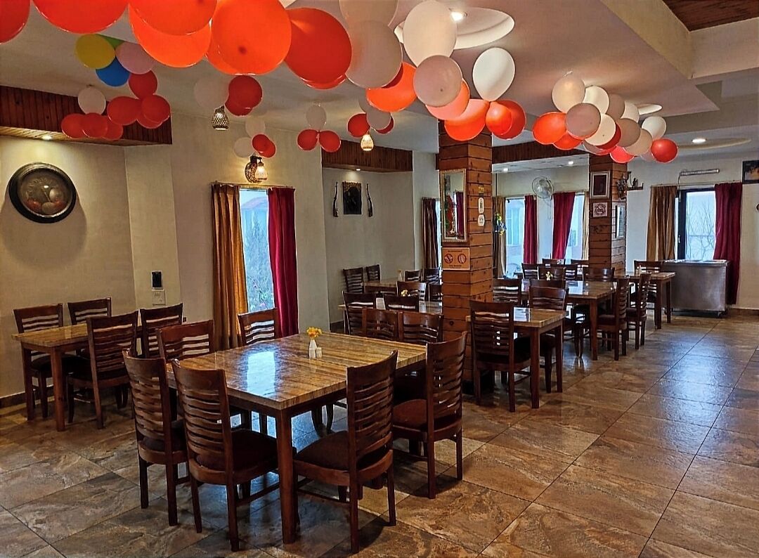 Ein Restaurant mit mehreren Holztischen und -stühlen, roten und weißen Luftballons, die von der Decke hängen, und einem Steinplattenboden.
