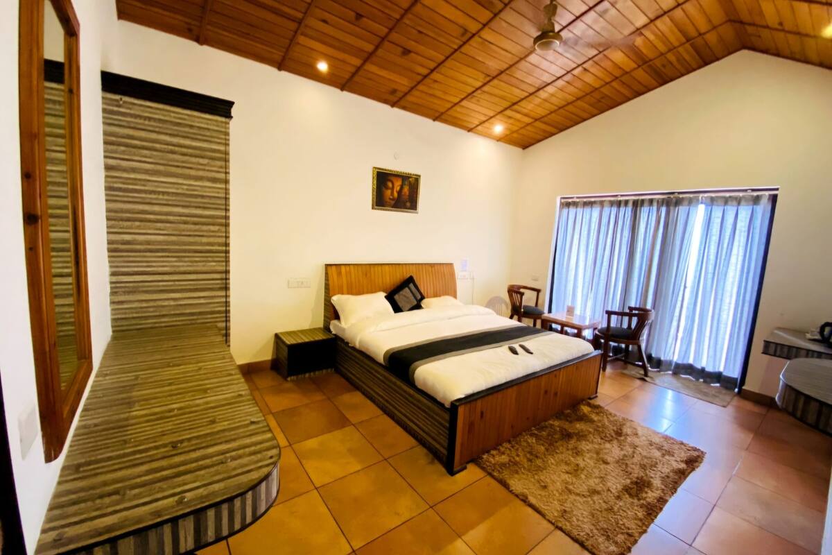 A bedroom with a wooden ceiling, a bed, a small table, a chair, and a window with curtains.