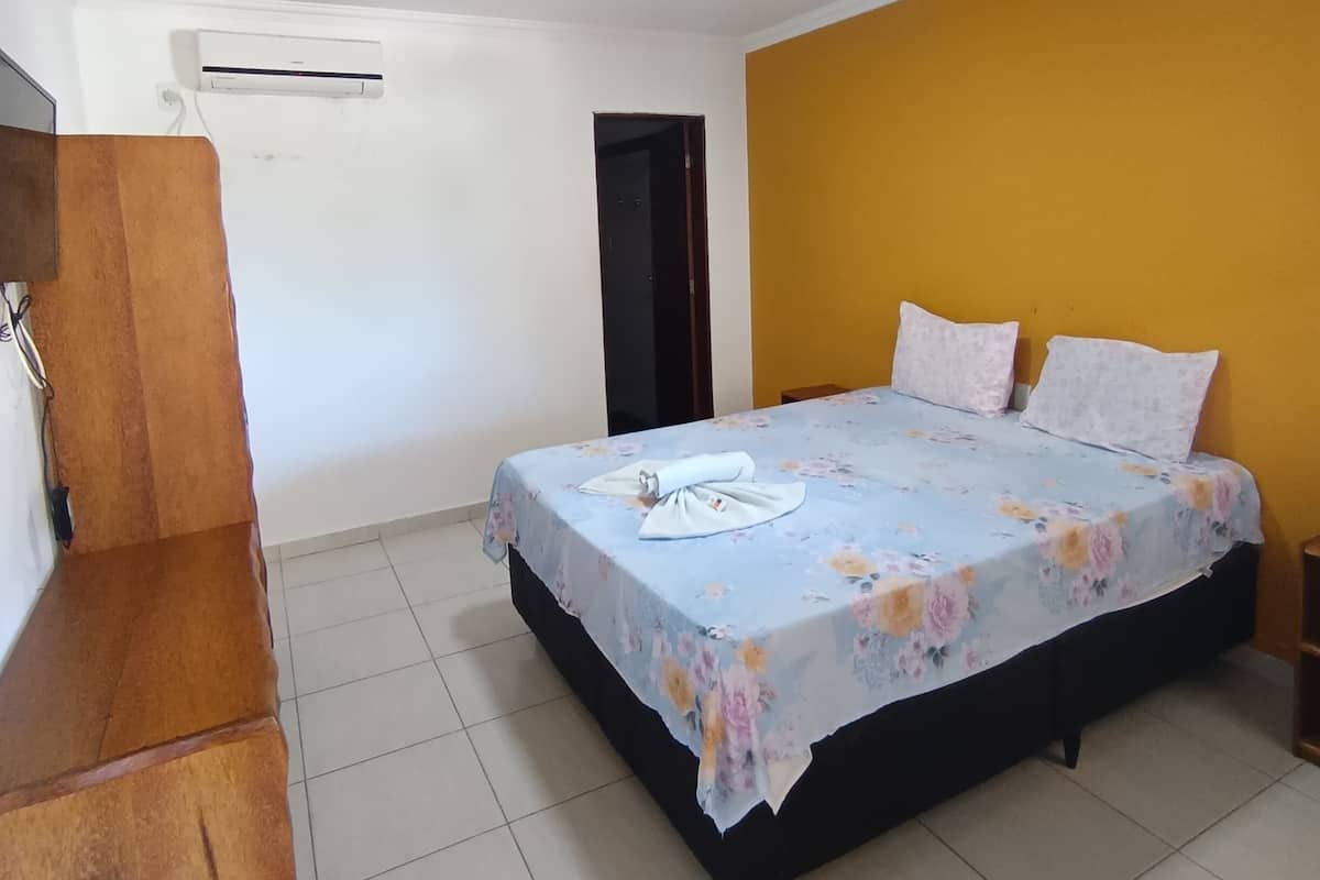 A bedroom with a bed, a wooden wardrobe, and an air conditioning unit.