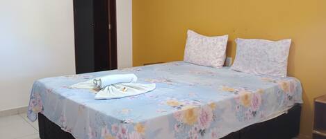 A bedroom with a bed, two pillows, a nightstand, and a door.
