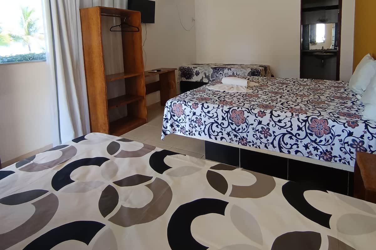 A bedroom with a bed, a wardrobe, a TV, and a window with curtains.