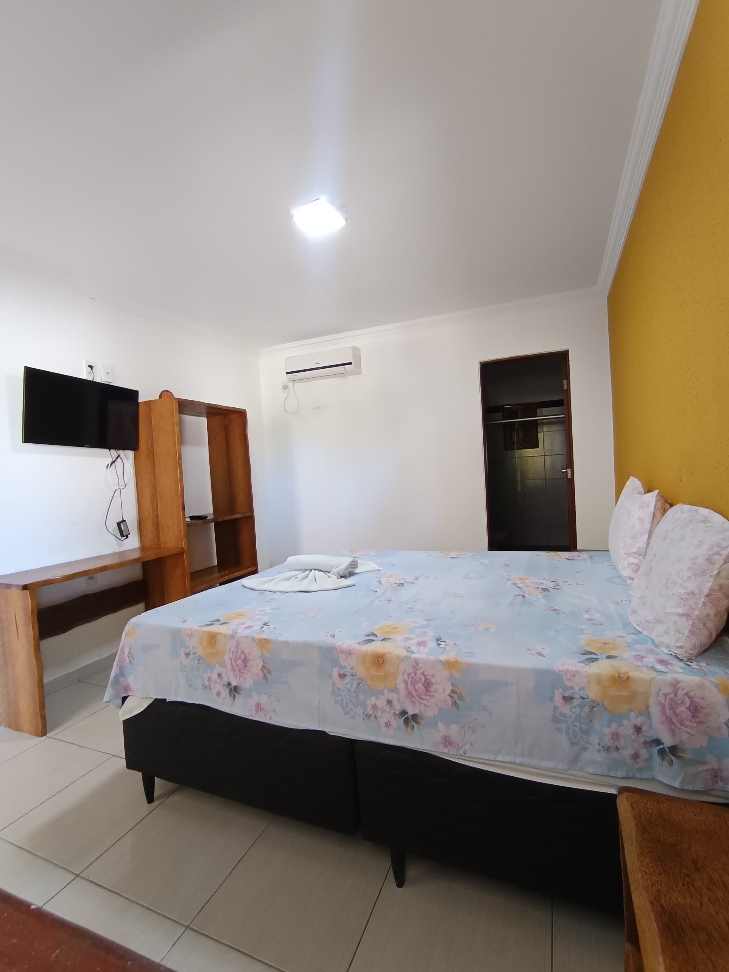 A bedroom with a bed, a TV mounted on the wall, a wardrobe, and an air conditioning unit.