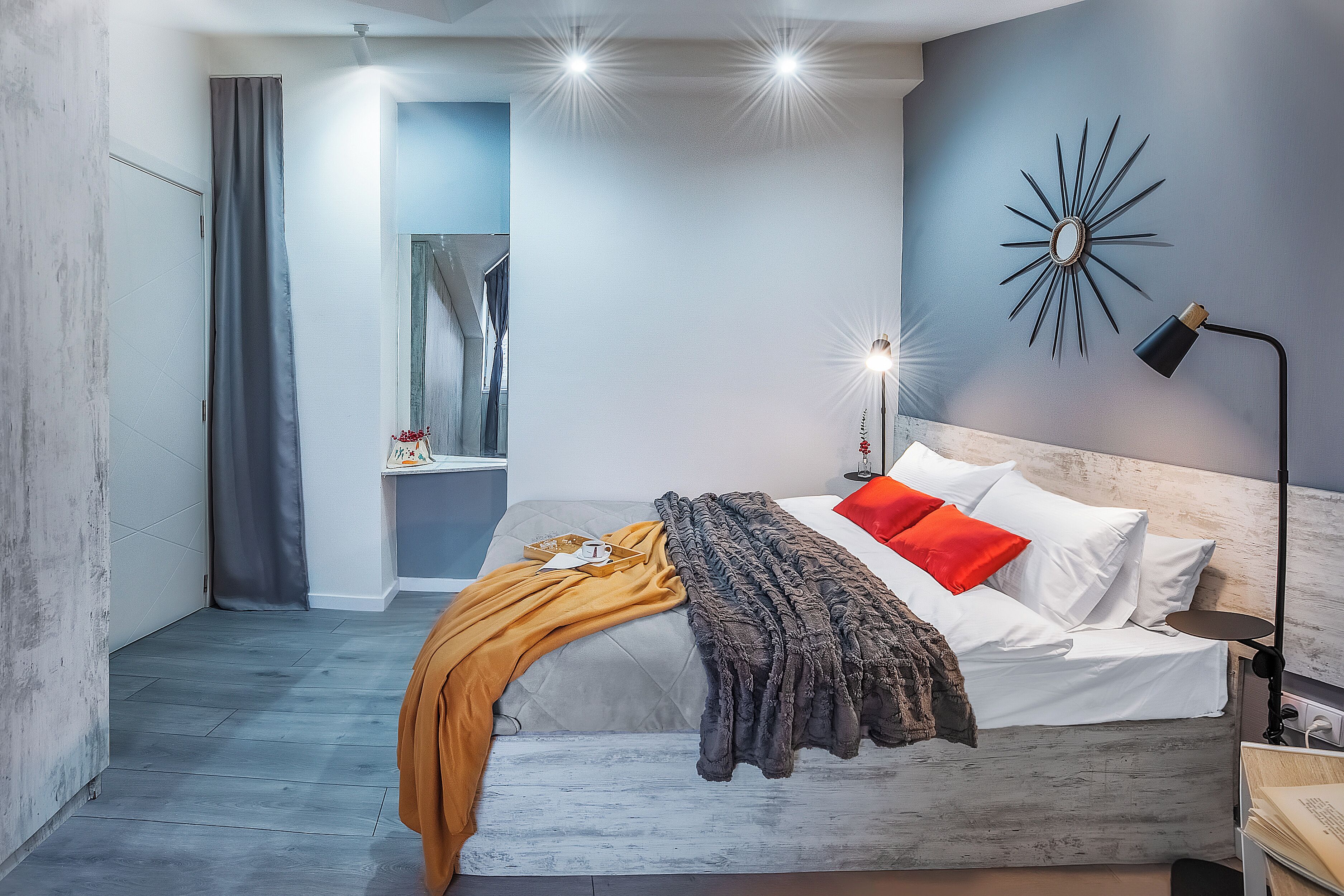 A modern bedroom with a bed, a nightstand, a wall-mounted lamp, and a decorative mirror.