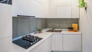 A compact kitchen with white cabinets, a gas stove, a sink, and a small countertop area with a plant and a coffee machine. - HB apartments Merab Kostava (Tbilisi)