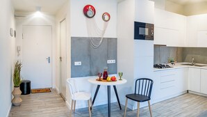 A modern kitchen with white cabinets, a microwave, and a gas stove. There is a dining area with two chairs and a small table with fruit and a glass. - HB apartments Merab Kostava (Tbilisi)