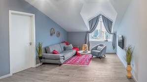 A modern living room with a grey sofa, red cushions, a coffee table, and a red rug. There are two side tables with plants, a grey armchair, and a window with curtains. - HB apartments Merab Kostava (Tbilisi)