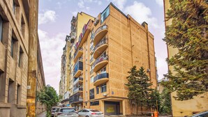 A multi-story residential building with balconies, a garage entrance, and parked cars along the street. - HB apartments Merab Kostava (Tbilisi)