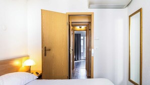A hotel room with a bed, a nightstand with a lamp, a wooden door, and a mirror on the wall. - Charming Apartement- 1br-4p- Geneve (Geneva)