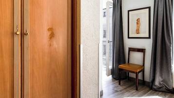 Une pièce avec une armoire en bois, une chaise en bois, un tableau encadré au mur et des rideaux gris.