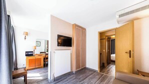 A hotel room with a wooden floor, a TV mounted on the wall, a bed, and a door leading to a bathroom. - Charming Apartement- 1br-4p- Geneve (Geneva)