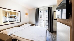 A hotel room with a bed, a flat-screen TV mounted on the wall, a window with curtains, and a framed picture on the wall. - Charming Apartement- 1br-4p- Geneve (Geneva)