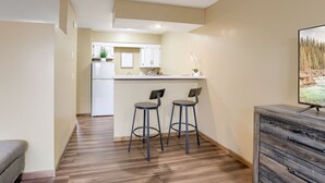 Cocina compacta con gabinetes blancos, un refrigerador blanco y una pequeña isla con taburetes.