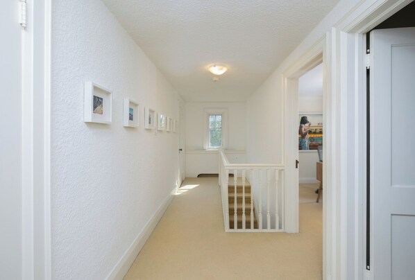 Een hal met witte wanden, een vloerbedekking, een trap met een witte leuning en een deur naar een andere kamer.