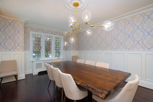 Une salle à manger avec une grande table en bois, six chaises, un lustre et un papier peint à motifs.