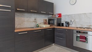 A modern kitchen with dark cabinets, a marble backsplash, and a clock on the wall. - Maltese Cozy Studio Apartment (SAN PAWL IL-BAĦAR)
