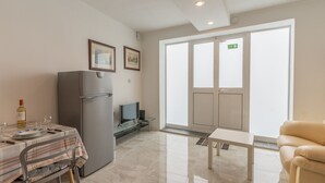 A modern kitchen with a refrigerator, a dining table set with plates and glasses, a television, and a sofa. - Maltese Cozy Studio Apartment (SAN PAWL IL-BAĦAR)